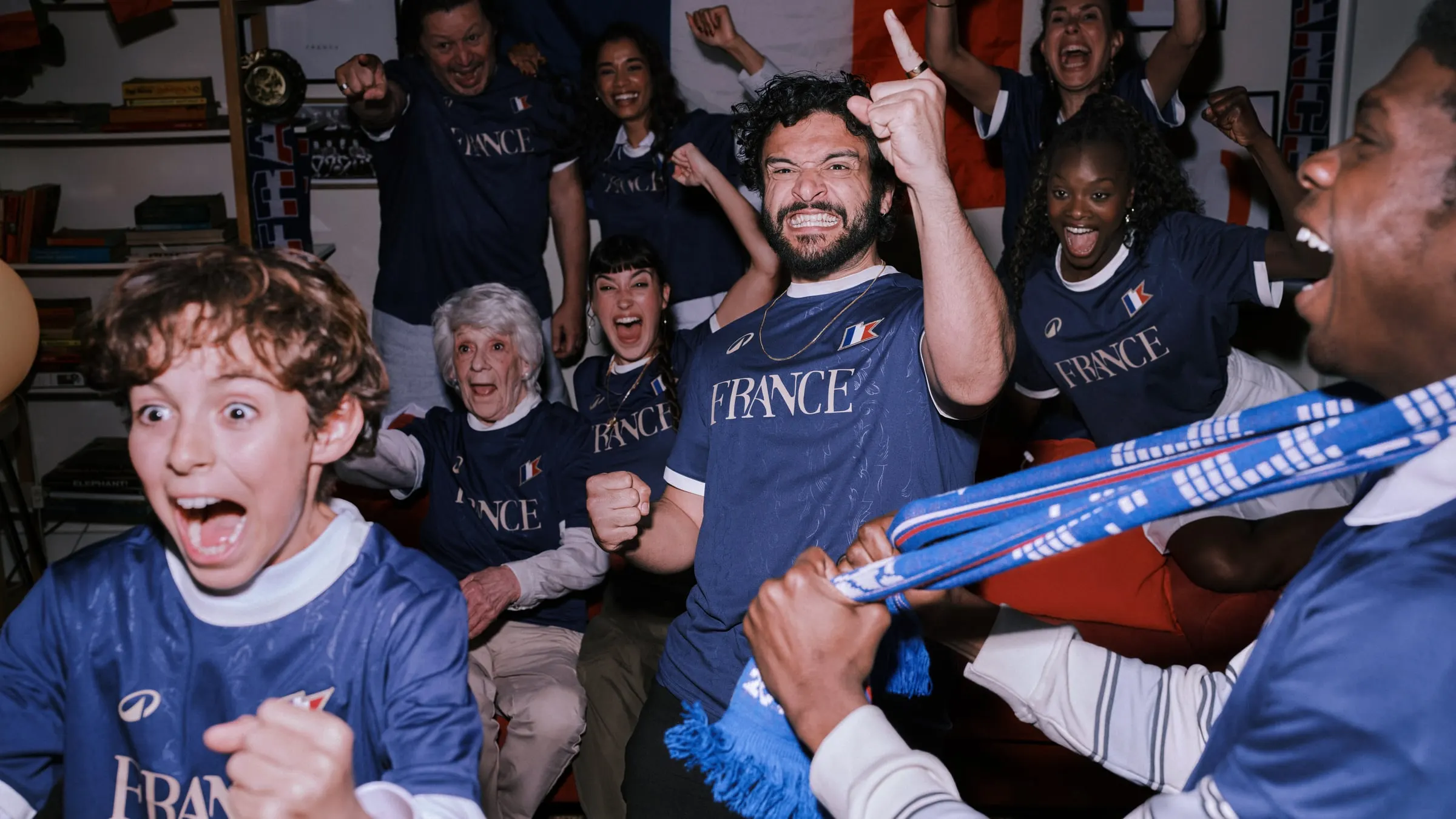 A family of France fans in navy kits erupting with joy in a living room