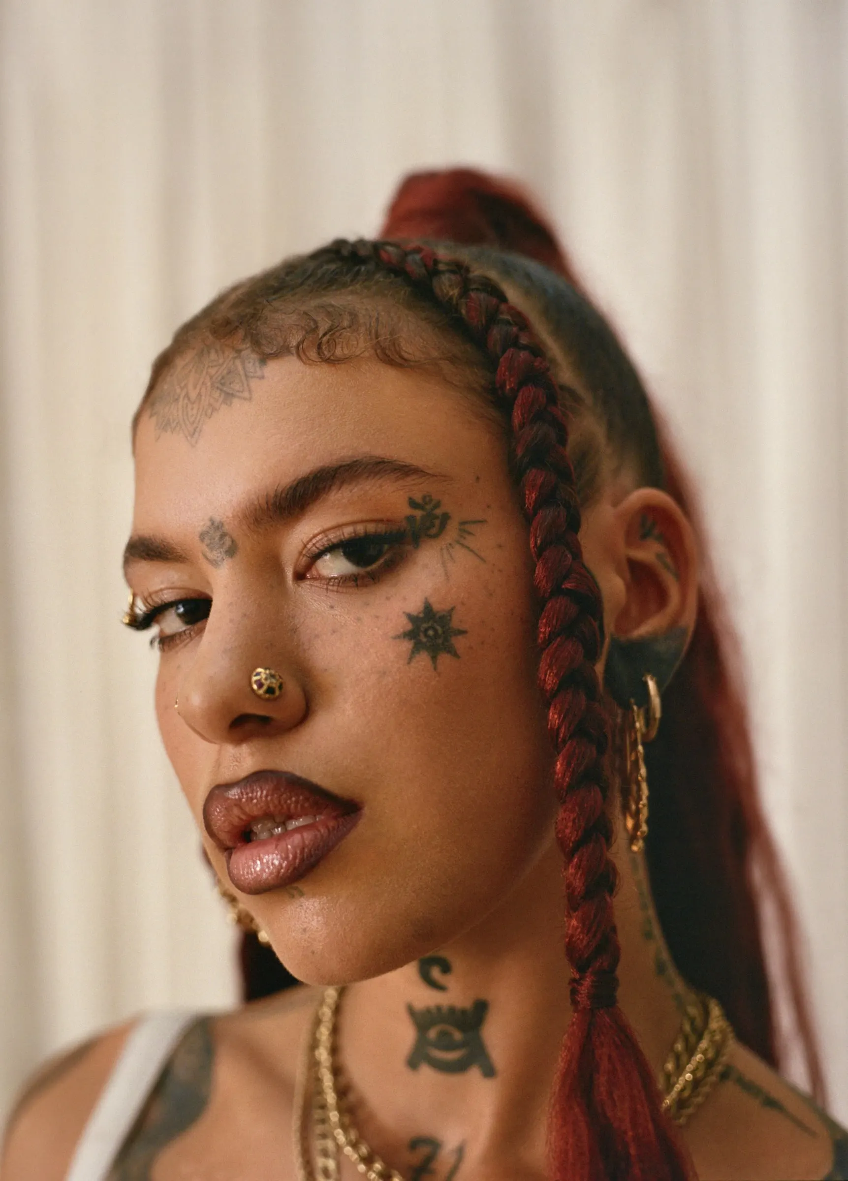 Close portrait of Greentea Peng with red braids, face tattoos, piercings and gold chains