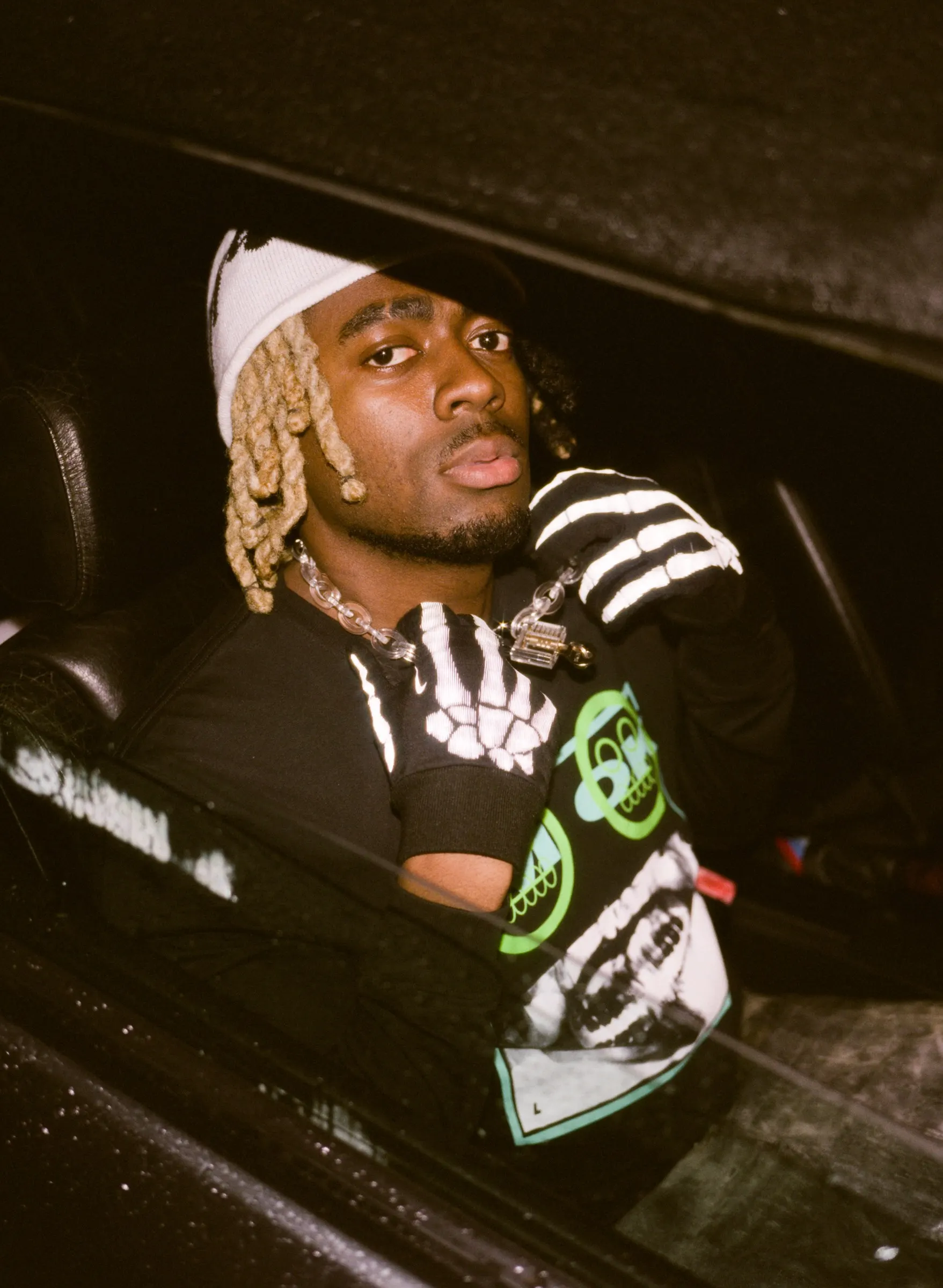 INFAMOUSIZAK leaning out of a car window at night in skeleton gloves