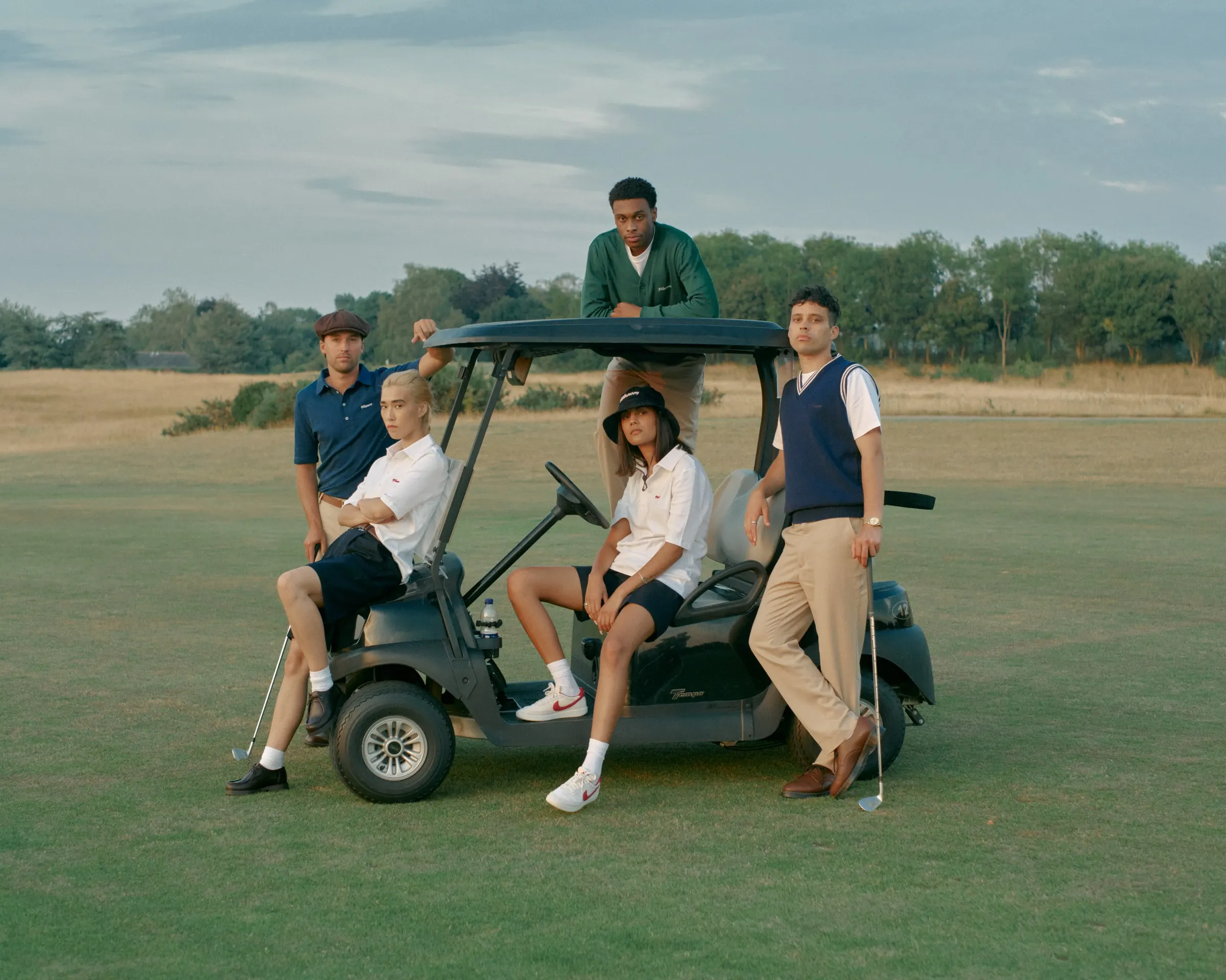 Friends in Manors gathered around and on top of a golf buggy on the fairway