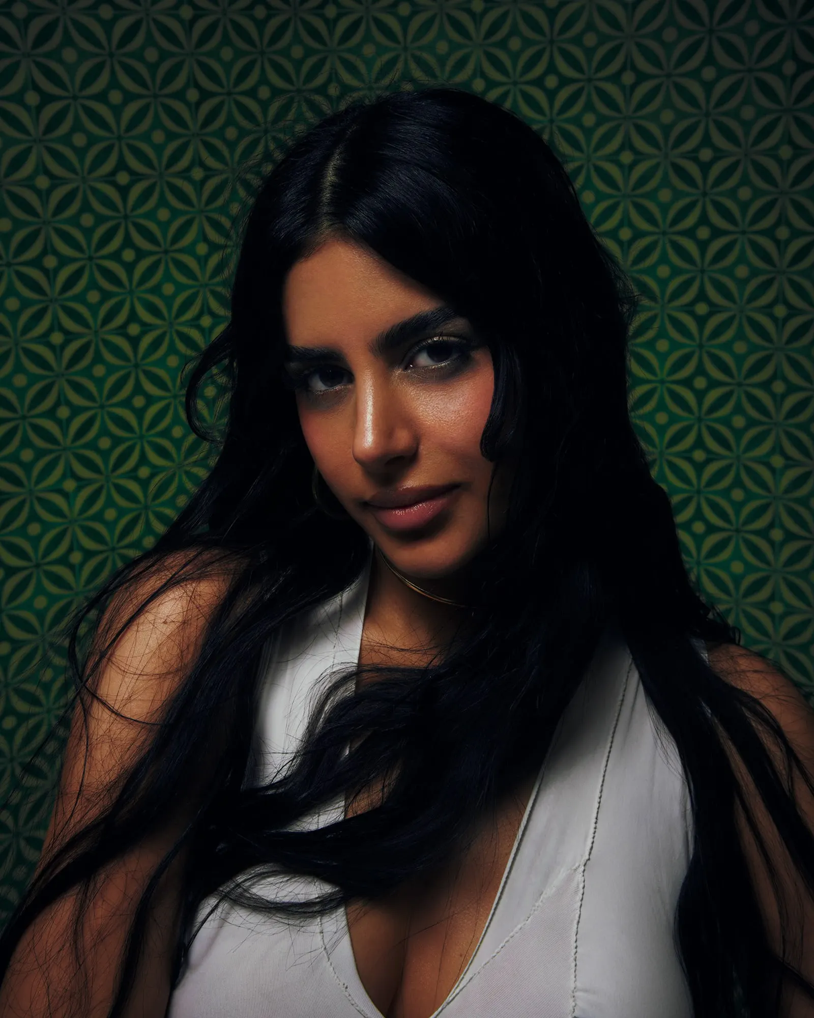 Close portrait of Maria Taktouk in a white top against green geometric wallpaper