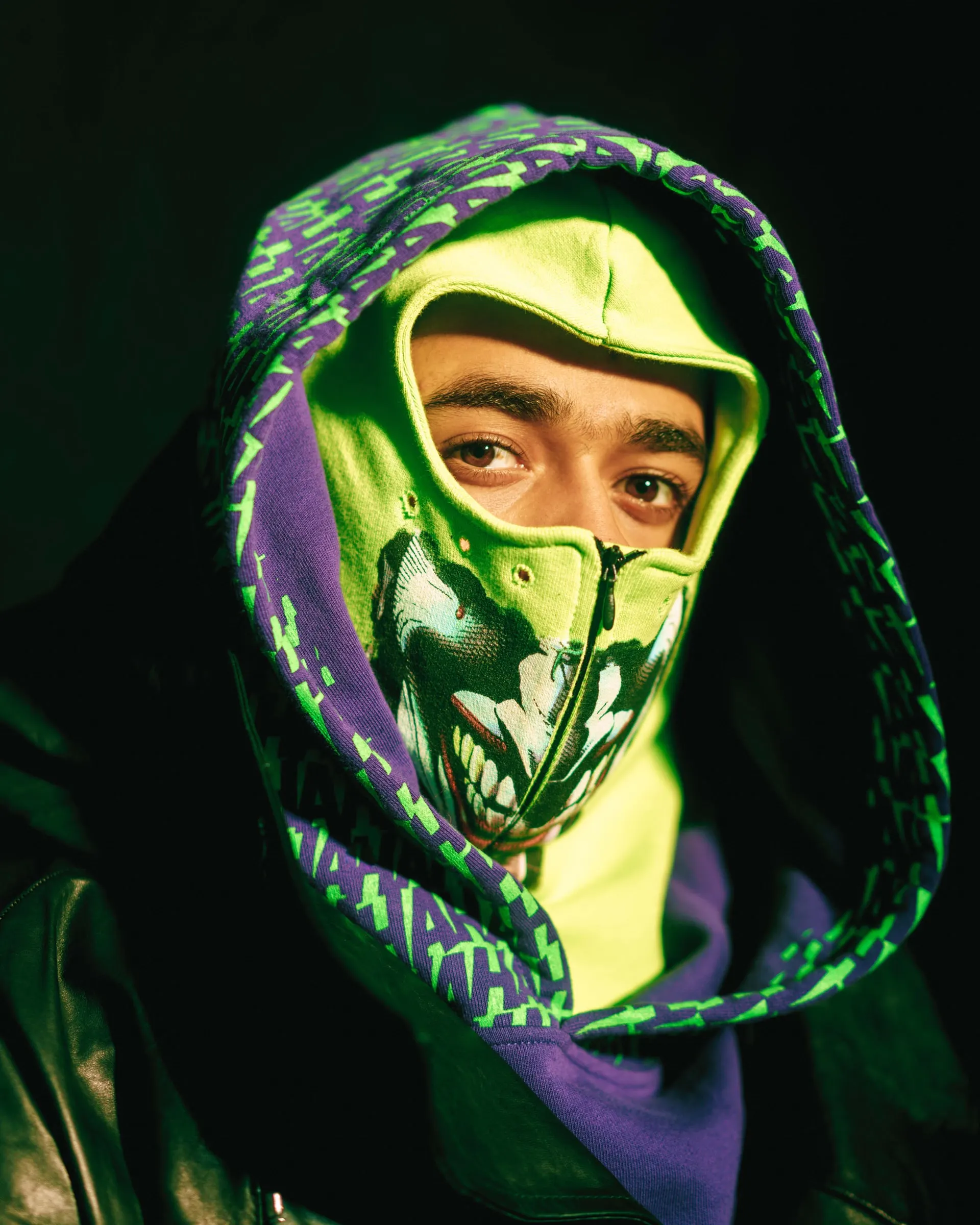 Nafe Smallz in a neon green and purple hood and printed face mask against a dark background