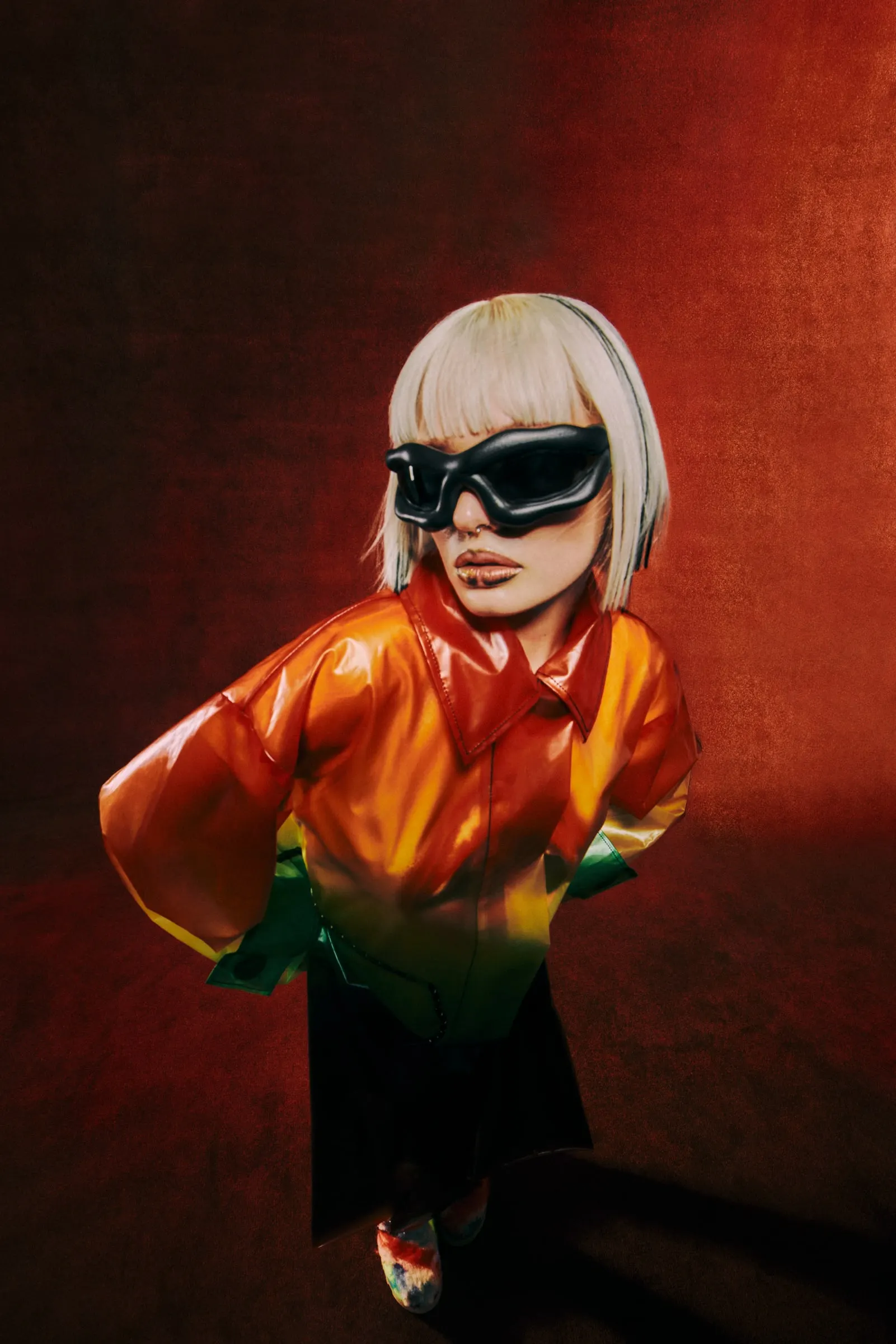 Rubi Ward crouched in black goggles and a glossy orange-to-green coat against a red backdrop