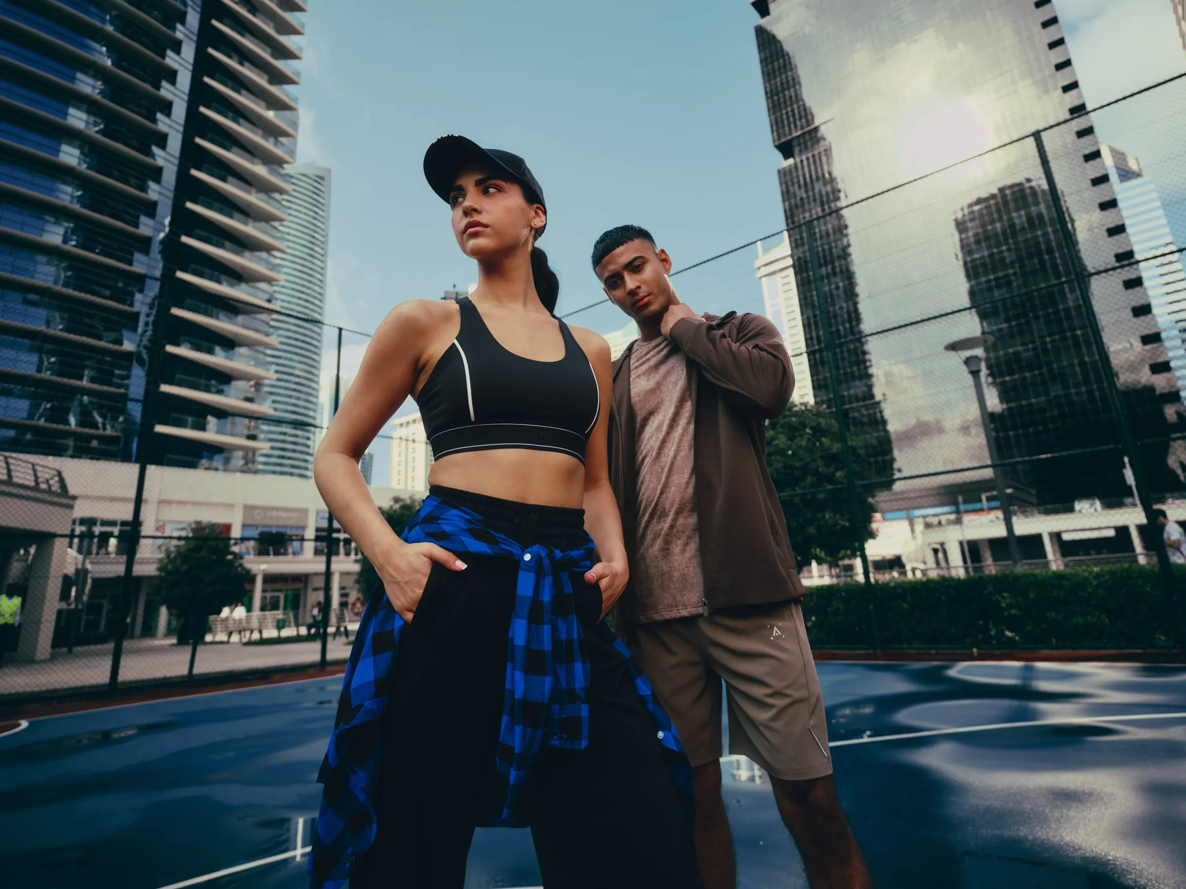 Two models in sportswear on a rooftop court among glass towers