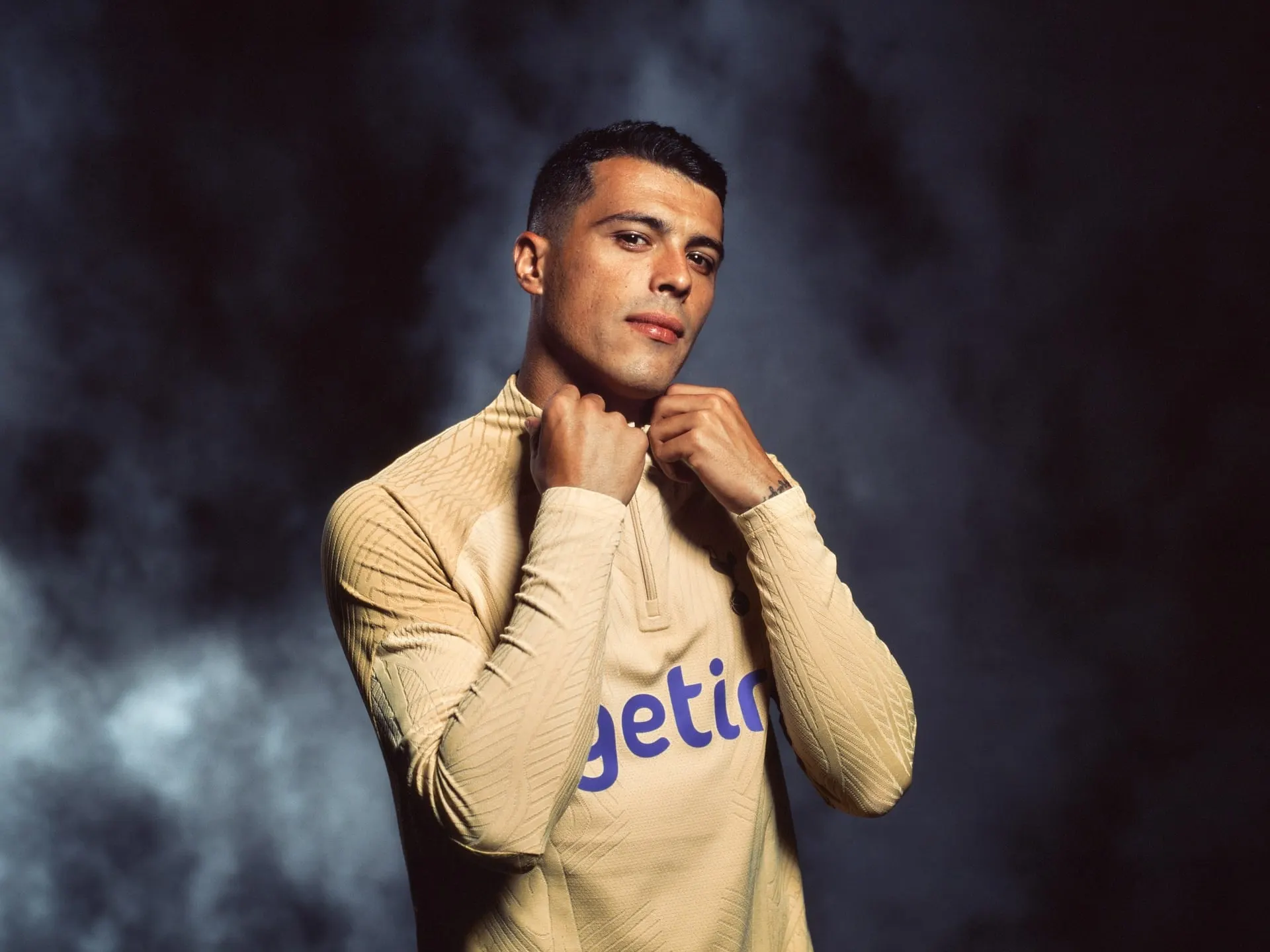 A Spurs player adjusting the collar of his gold training top in low light