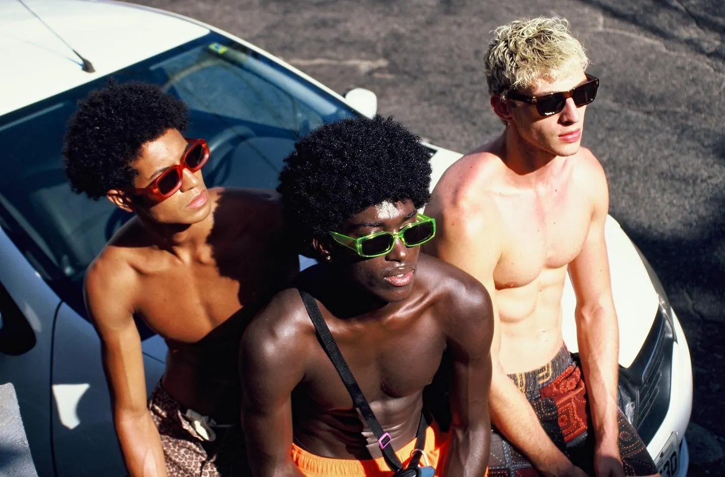 Three friends in sunglasses sitting on the bonnet of a white car in the Rio sun
